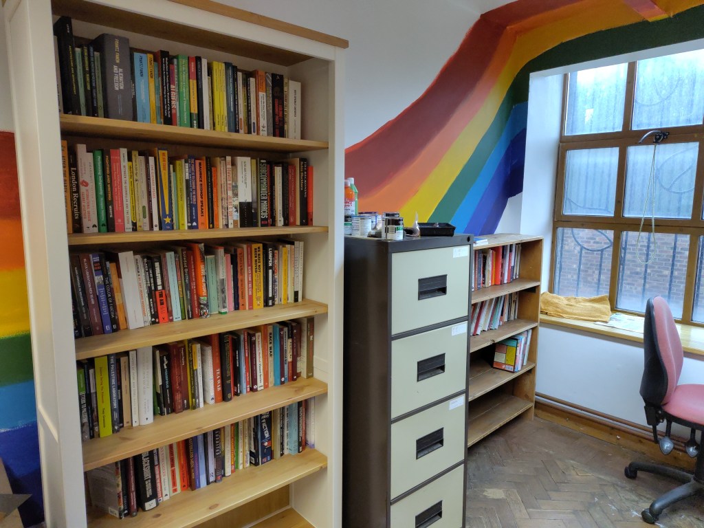 Shelves of books with a rainbow painted on the wall behind them.